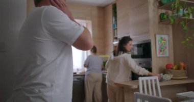 Modern mutfakta birlikte yemek hazırlayan bir grup insan, sıradan aile ortamları, kapüşonlu kadınlara odaklanma, yemek pişirme anlarının sıcak atmosferi.