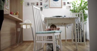 Çocuk bir sandalyenin yanında çömelmiş, yemek odasında oyuncak bir arabayla oynuyor aile dekorasyonları, ahşap döşemeler ve sıcak bir ev atmosferi var.