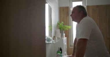 Lavaboda duran, öne doğru eğilen, yansıtıcı ve sakin bir ifade, doğal ahşap banyo detayları, huzurlu bir ortamda tımar sonrası an