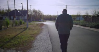 Sessiz bir banliyö caddesinde yürüyen bir adam, arkadan görüldü, açık hava aktivitesi, yalnızlık ve huzurlu mahalle çevresi üzerine odaklandı.
