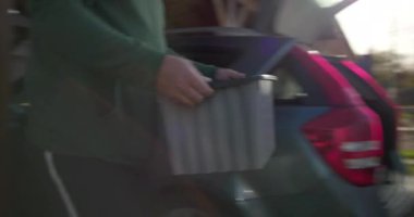 Bir adam plastik bir kutu taşıyor ve onu açık hava arabasının bagajına koyuyor. Organizasyon için hazırlanıyor, ev işleri yapıyor ya da açık hava ortamında seyahat ediyor.