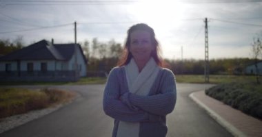 Bir banliyö caddesinde rahat bir eşarbı sımsıkı sarıp sıcacık gülümseyen bir kadın, huzurlu bir mahalle ortamında sakin bir anın tadını çıkarıyor.