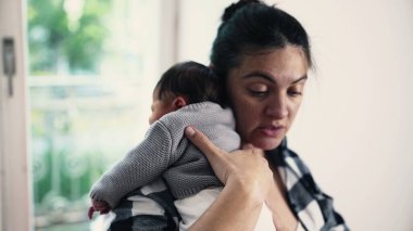 Anne, yeni doğmuş bebeğini emzirdikten sonra omzuna koyuyor, güneşli bir odada sessiz bir bağ kurma ve bakım anı yakalıyor. Bebek annesinin üzerinde huzur içinde yatıyor.