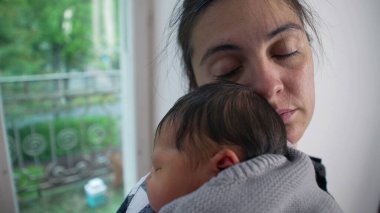 Anne, yeni doğmuş bebeğini omzuna almış, gözleri dingin bir şekilde bağlanmış. Anne ve çocuk arasındaki derin bağ ve sıcaklık.