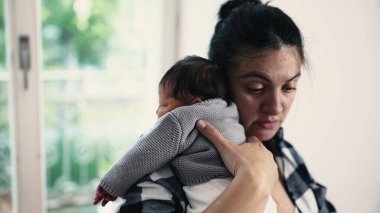 Anne, yeni doğmuş bebeğini emzirdikten sonra omzuna koyuyor, güneşli bir odada sessiz bir bağ kurma ve bakım anı yakalıyor. Bebek annesinin üzerinde huzur içinde yatıyor.