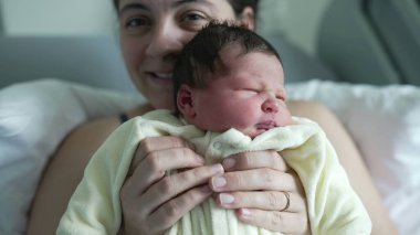 Anne yeni doğmuş bebeğini neşeyle hastanede tutuyor. Anne 'nin gururlu gülümsemesi ve bebek içerikli ifadesi annelik sevgisinin ve bağlantının hassas bir anını yakalar.