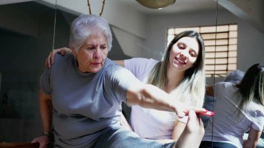 Kadın Pilates Koçu yaşlı yaşlı bir kadının fizik tedavi seansında bacaklarını esnetmesine yardım ediyor.. 