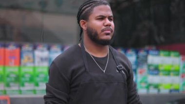 Önlüklü bir adam güvenle boya dükkanının önünde duruyor. Kararlı ve profesyonel görünüyor. Perakende satış elemanı olarak rolünü sergiliyor.