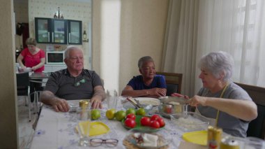 Bir grup yaşlı arkadaş samimi, sıradan bir ev ortamında öğle yemeği için toplandı. Oturma odasında çeşitli yaşlılar konuşuyor..