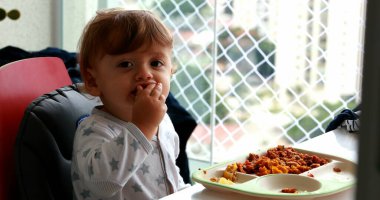 Bebek yemek yiyor, sandalyede oturuyor.