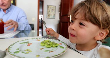 Çocuk kivi meyvesi yiyor. Küçük çocuk meyveli tatlı yiyor.