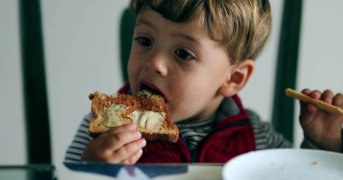 Çocuk tereyağlı kahvaltı ile tost yiyor.