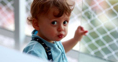 Bebek bebek pencereye yaslanmış, güvenlik çitleriyle dışarı bakıyor.