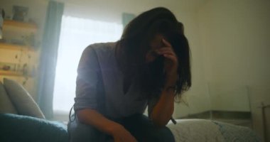 Elleriyle yüzünü kapatan bir kadın duygusal karmaşadan, kayıplardan, kalp kırıklıklarından ve derin kişisel mücadelelerden etkilenmiş bir şekilde oturuyor.
