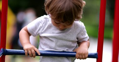 Küçük çocuk oyun parkında çitlere tırmanıyor. Çocuk aşağı iniyor.