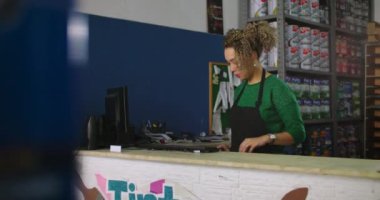 Bir hırdavatçıda tezgahta çalışan odaklanmış genç bir kadın, arka planda düzenli raflar olan bir bilgisayarda daktilo yazıyor.