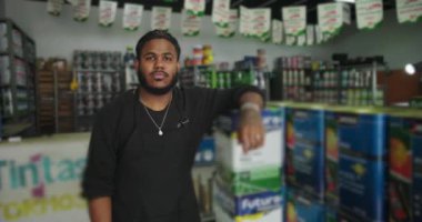 Kendine güveni tam bir tezgahtar hırdavatçıdaki boya kutularına yaslanıyor. Organize bir ortamda boya malzemeleriyle müşteri hizmetlerini sergiliyor.