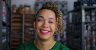 Bir hırdavatçıda gülümseyen kadın girişimcinin yakın çekimi, arka planda boya ve malzeme rafları ile güven ve pozitiflik yayıyor.