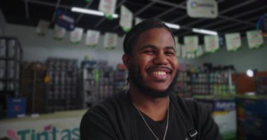 Arka planda bulanık boya kutuları ve malzemelerle çevrili bir boya dükkanında siyah önlüklü bir adamın sıcacık gülümsemesi.