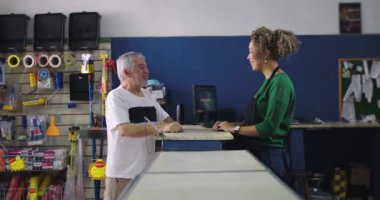 Esnaf ve yaşlı müşteri bir hırdavatçıda tezgahta sohbet ediyorlar, bağlantıyı teşvik ediyorlar ve mükemmel müşteri hizmetleri sunuyorlar.