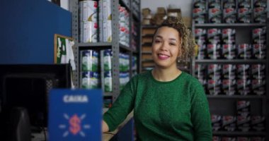 Etrafı boya ve malzemelerle çevrili bir hırdavatçıda güvenle gülümseyen genç bir kadının yakın çekimi profesyonelliği ve misafirperver bir tavrı temsil ediyor.