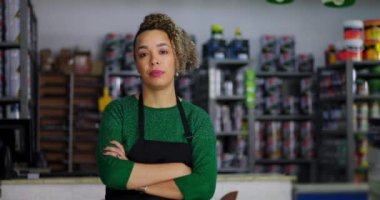 Bir hırdavatçıda kolları çapraz duran ciddi bir esnaf, arka planda renkli ürünlerle dolu raflar, modern küçük işletme sahibi portresi