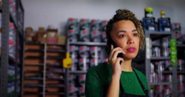 Dükkan sahibi, organize ürün raflarıyla çevrili bir hırdavatçıda müşterilerin ihtiyaçlarına dikkat çekmek için telefonda detayları tartışıyor.