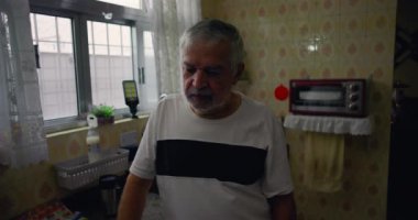Mutfakta duran yaşlı bir adam, düşüncelere dalmış, evcil ortamda yalnızlığı ve sessizliği yansıtıyor.