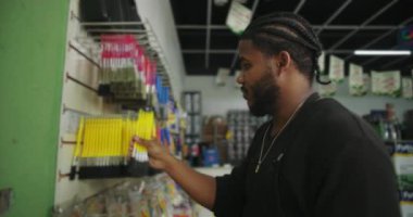 Siyah önlüklü bir adam boya dükkanındaki bir rafa boya fırçalarını yerleştiriyor, renkli fırçaları ve aletleri raflarda sergilenen malzemeleri organize etmeye odaklanıyor.