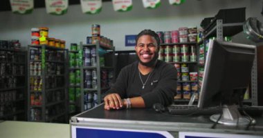 Boyacıdaki adam tezgahta güvenle gülümsüyor, masada bir bilgisayar ve arka planda canlı boya kutuları var.