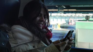 Tren penceresinin yanında cep telefonu cihazını tutan mutlu kadın.