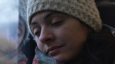 Trende Uykudan Uyanan Kadın, arka planda manzara geçerken gözlerini açan bir kadın yolcunun yakın görüntüsü.