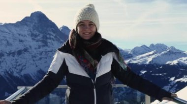 Karla kaplı İsviçre Alplerine tepeden bakan mutlu bir kadın ve kışlık giysiler giyip güzel dağ manzarasının tadını çıkarıyor.