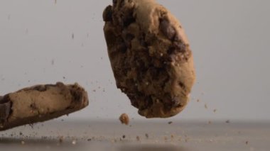 Çikolata parçacıklı kurabiyeler masanın yüzeyine düşüyor ve havada uçuşan kırıntılarla çarpışmayı çok yavaş çekimde yakalıyor.