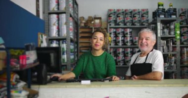 Gülümseyen adam ve kadın, organize boya ve araç gereçlerle çevrili yerel küçük işletme nalbur dükkanının tezgahında yan yana duruyorlar.