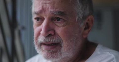 Yaşlı adam parmaklıkları sıkıca kavrıyor, sıkıntı ve derin düşünce gösteriyor, duygusal ve yansıtıcı ifade, yalnızlık ve derin tefekkür tasviri.