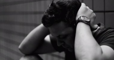 Başı aşağıda oturan bir adamın yakın çekimi, elleri başının üstünde, duygusal içgözlem, yansıtıcı an, şehir ortamı, dramatik ve düşünceli ruh hali, siyah ve beyaz