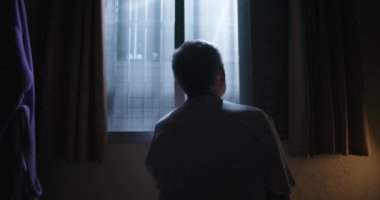 Karanlık bir odada oturan yaşlı bir adam, ay ışığıyla aydınlatılmış pencereye bakıyor, sessiz yalnızlık ve derin iç gözlem ile sarmalanmış.