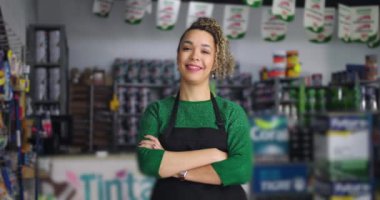 Canlı yerel hırdavatçıda kolları bağlı gülümseyen bir kadın. Etrafı ürün ve aletlerle çevrili. Kendine güveni tam ve sıcak bir tavırla dolu.