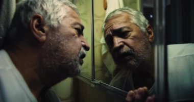 Yaşlı adam gözlerini banyodaki aynaya kilitledi. Yüzü kederle oyuldu. Cevaplar ve kefaret arayışında.