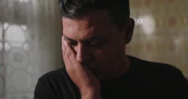 Bir eliyle yüzünü kapatan bir adam, gözleri kapalı, derin duygular ya da yansıma ifade eden, sakin bir atmosferde fayanslı duvarları olan eski mutfak dekoruyla çevrili bir adam.