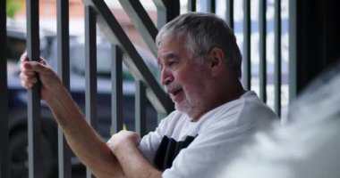 Parmaklıkları tutan yaşlı adam, keder ve acıyla dolu gözler, derin kayıp ve duygusal umutsuzluğu yansıtan, yalnızlığın dramatik tasviri ve zihinsel sağlıkla mücadele