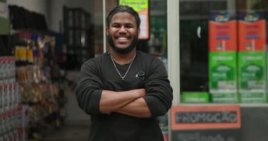 Satış mağazasının önünde kollarını kavuşturmuş, gülümseyen, gururlu ve profesyonel çevrede liderlik yapan kendinden emin genç bir zenci.