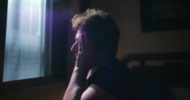 Pencere kenarında oturan yaşlı kadın elleri yüzün üzerinde dinleniyor. Endişe ve umutsuzluk hissediyor. Huzurlu, kapalı bir ortamda yalnızlık anı.