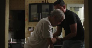 Oğlu, yaşlı babasına bunama ya da yaşla ilgili hastalıklarda yardım ediyor. Mutfaktaki sandalyeden kalkıp yatak odasına girmeye hazırlanırken ona destek oluyor.