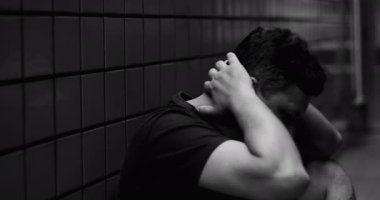 Duvara yaslanmış bir adam, kafası ellerde, yansıtıcı an, duygusal içgözlem, kentsel çevre, yalnızlık ve kişisel mücadele