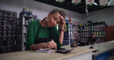 Küçük bir iş tezgahında mali hesaplar yaparken hayal kırıklığına uğramış görünen kadın girişimci, perakende satış ortamında mali zorlukları yönetiyor