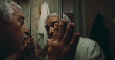 Adam aynaya karşı ıstırapla bastırılmış, yüzü öfkeyle ve umutsuzlukla bükülmüş, elleri cama kenetlenmiş, iç karışıklığı somutlaştıran, saf duygu, ve dramatik bir yardım çığlığı.