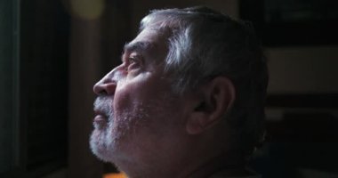 İçerde otururken, huzurlu ve düşünceli, sakin bir atmosferde, derin düşüncelere dalmış yaşlı bir adamın bakışlarının yakın plan profili.