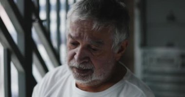 Aşağı bakan yaşlı bir adam, derin düşüncelere dalmış, keder ve duygusal yorgunluğun ağırlığı altında ezilmiş.